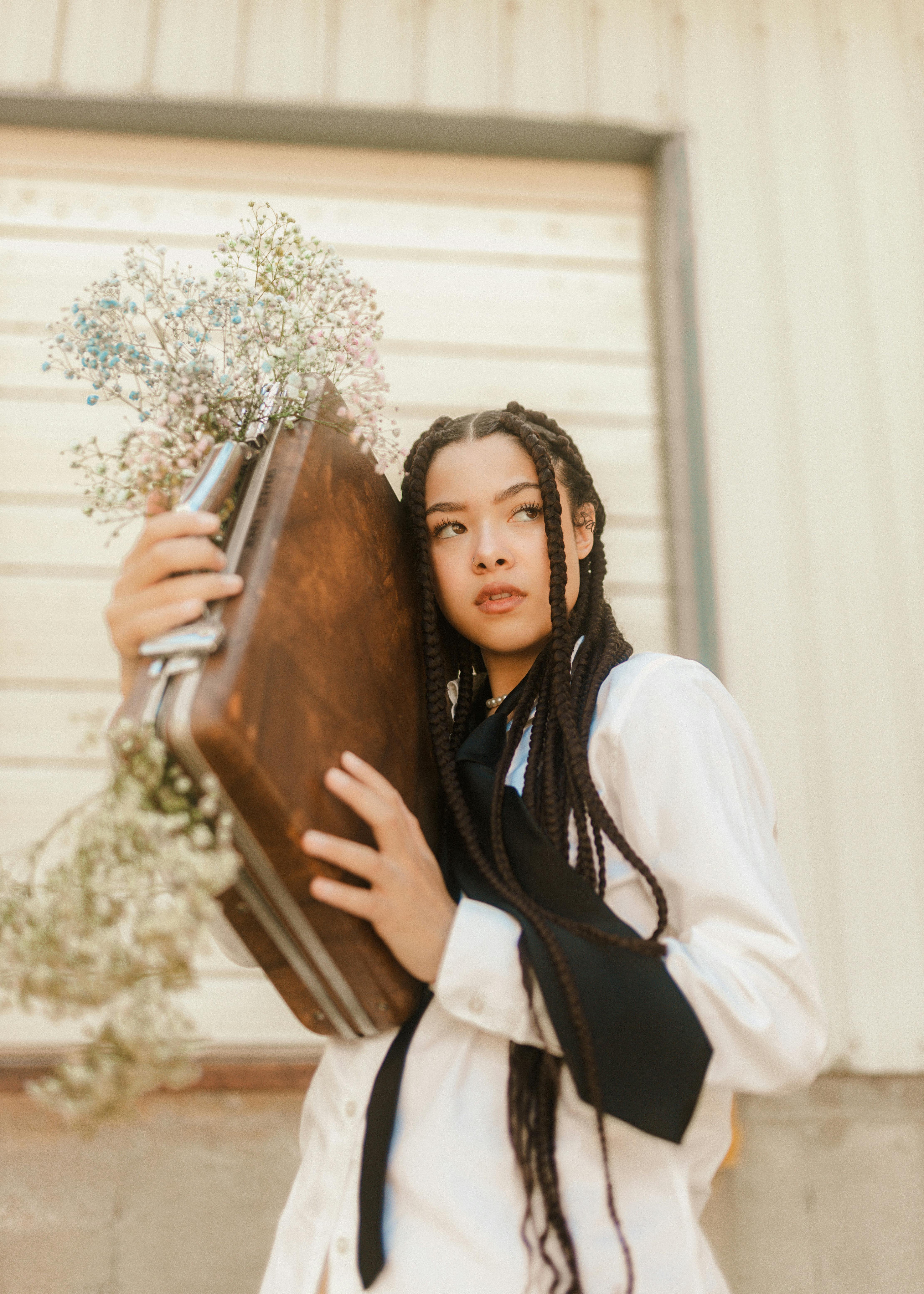 Young woman in Des Moines poses with a suitcase and flowers, showcasing a unique hairstyle.