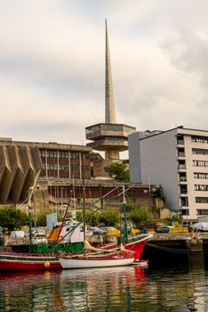 Colorful boats docked at a vibrant urban waterfront under a distinctive spire.