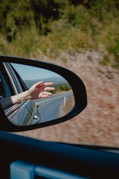 Capture the essence of travel with a hand out the window and a scenic road view in the mirror.