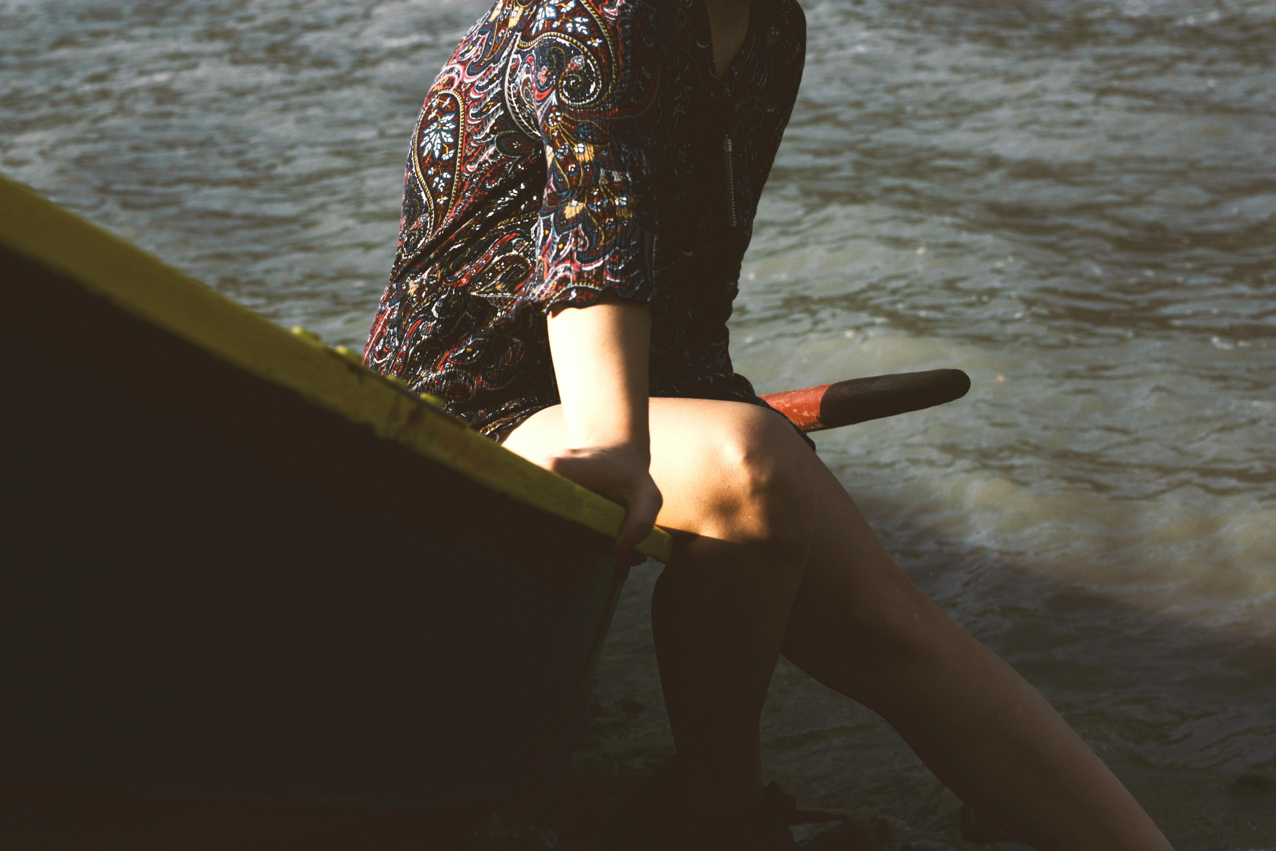 一名女子身穿彩色佩斯利连衣裙，坐在河边的船上