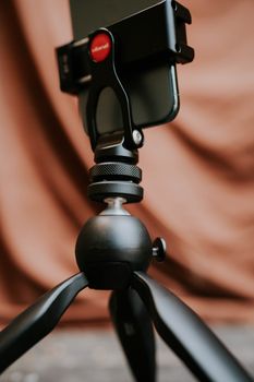 Close-up of a smartphone mounted on a tripod against a soft brown background, highlighting modern photography equipment.
