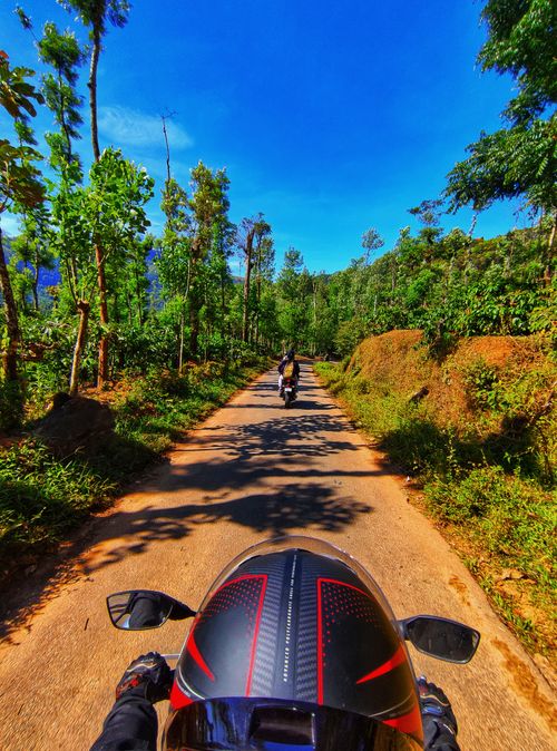 Free Motorcyclists ride through a scenic unpaved road surrounded by lush green trees in Balige, India. Stock Photo