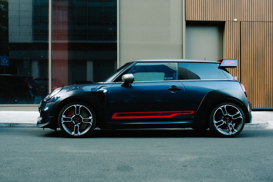 A sleek Mini Cooper with striking red accents parked on an urban street with modern architecture.