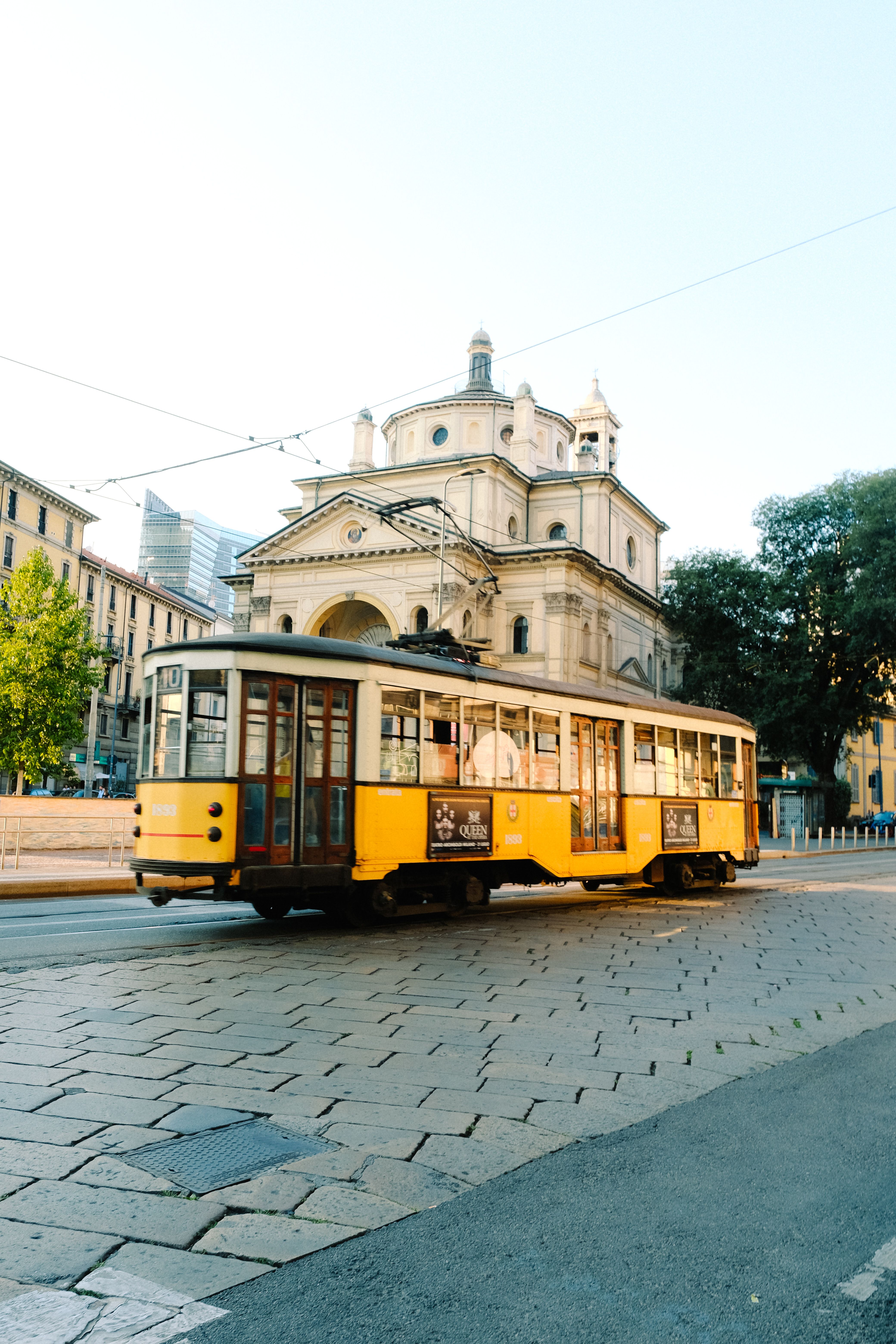 A quaint yellow tram passes by a historic church in Milan on a sunny day.