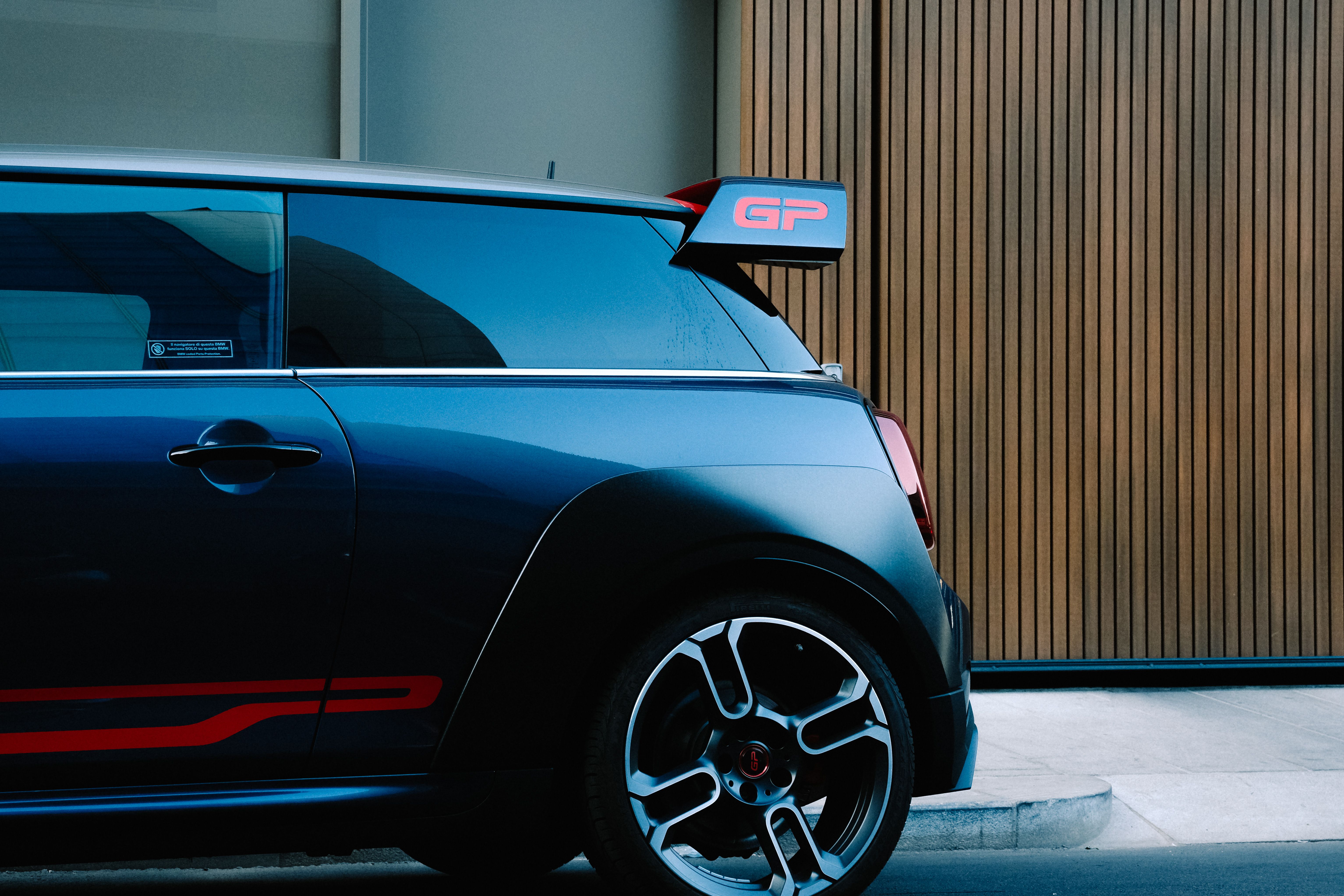 A stylish black Mini Cooper parked beside a modern wooden wall, showcasing sleek design and urban aesthetic.