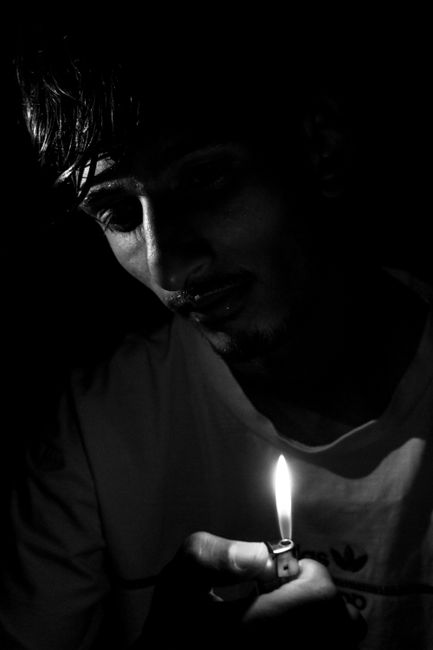 Dark, mysterious black and white portrait of a man holding a lighter in low light.