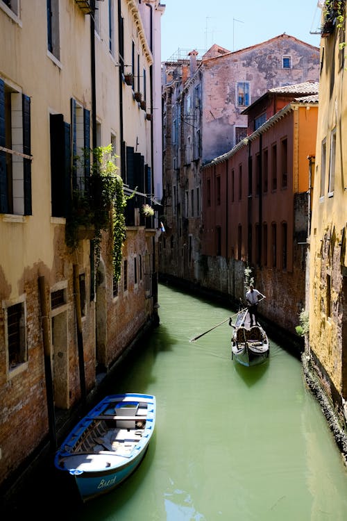 A Boat on River Between Brown Concrete Buildings