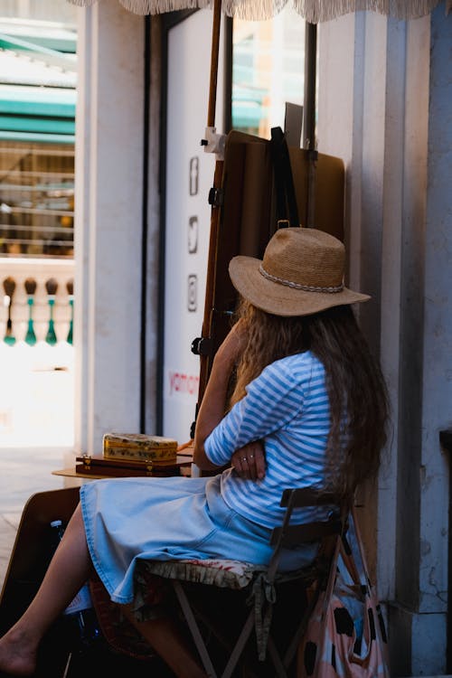 Woman in Blue and White Stripe Long Sleeve Shirt and Brown Cowboy Hat Sitting on Chair
