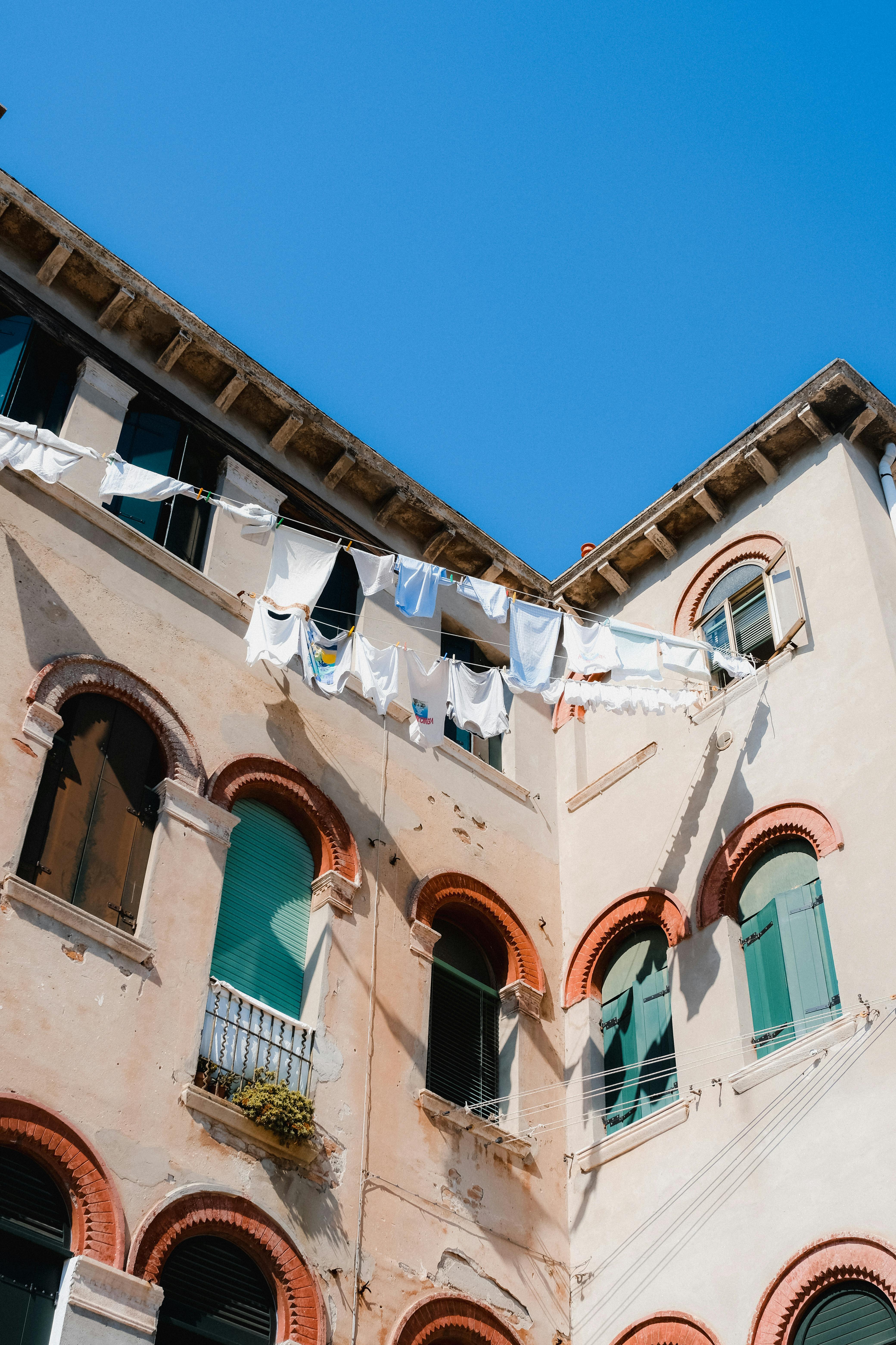 Laundry hanging outside a charming Italian building under a clear blue sky.