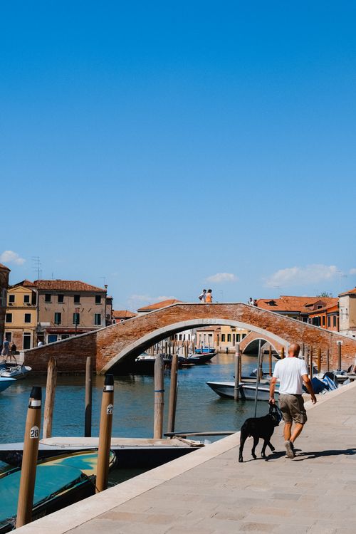 Free A charming view of Venice with a traditional brick bridge over a canal, under a clear blue sky. Stock Photo
