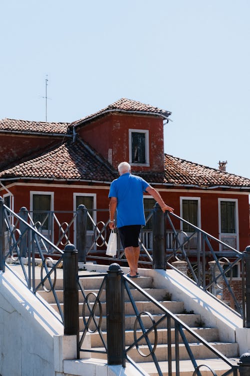 Man in Blue Shirt Walking on Concrete Stairs With Metal Railings