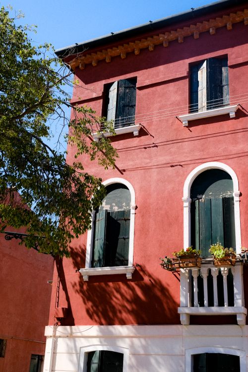 Free Red house exterior with shutters and a small balcony under clear blue skies, showcasing urban architecture. Stock Photo