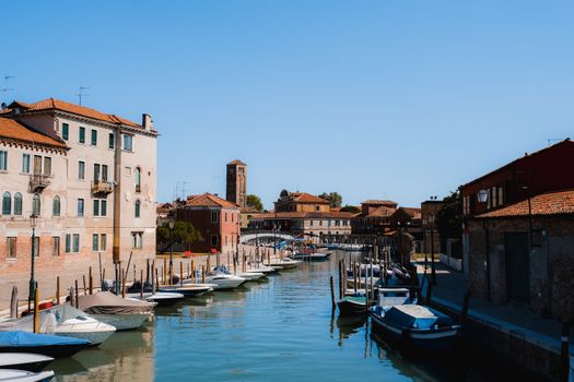 Picturesque view of boats moored along a canal in Venice with historic buildings under a clear blue sky.