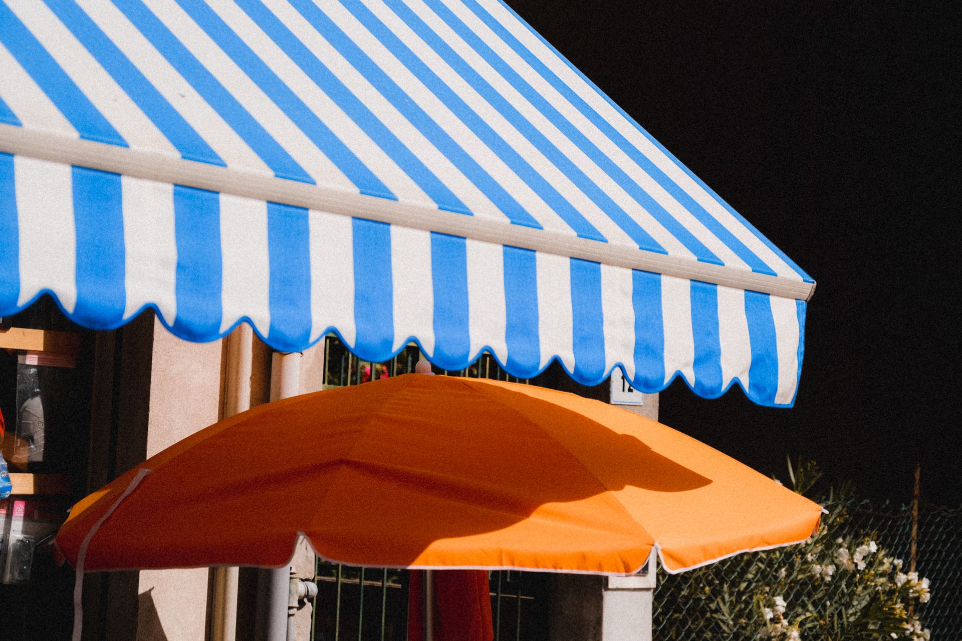 Vibrant blue striped awning and orange umbrella providing summer shade outdoors.
