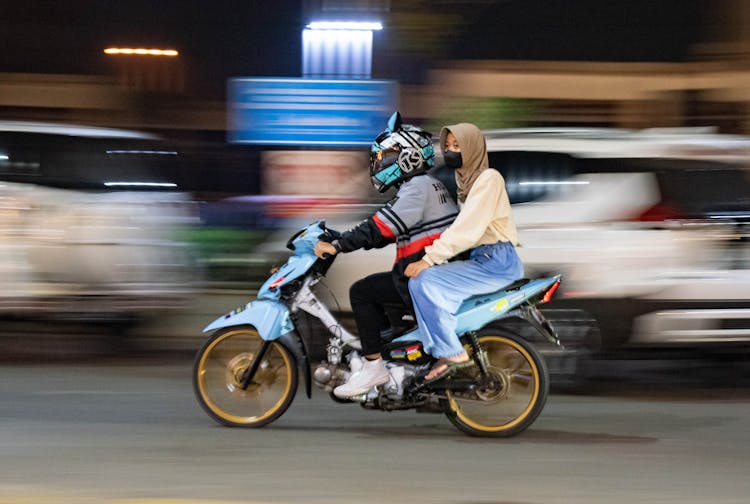 Man Wearing A Helmet And Woman Wearing A Headscarf Riding Together On A Motorbike 