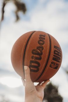 A close-up shot of a hand holding a basketball against a clear sky, ideal for sports themes.