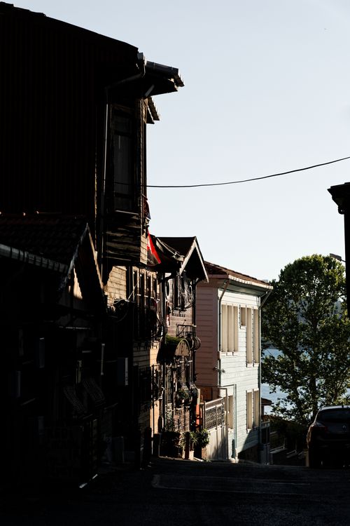 Free Glimpse of a narrow street lined with wooden houses, casting shadows, under a clear sky. Stock Photo