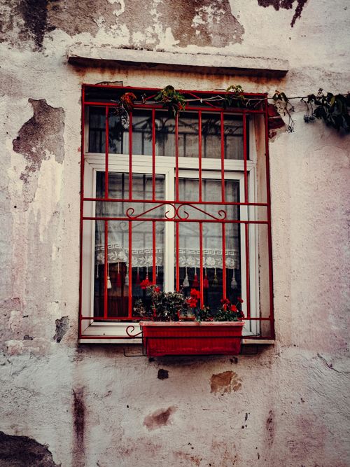 Free Charming rustic window with red iron bars and floral box on a weathered wall, evoking vintage aesthetics. Stock Photo