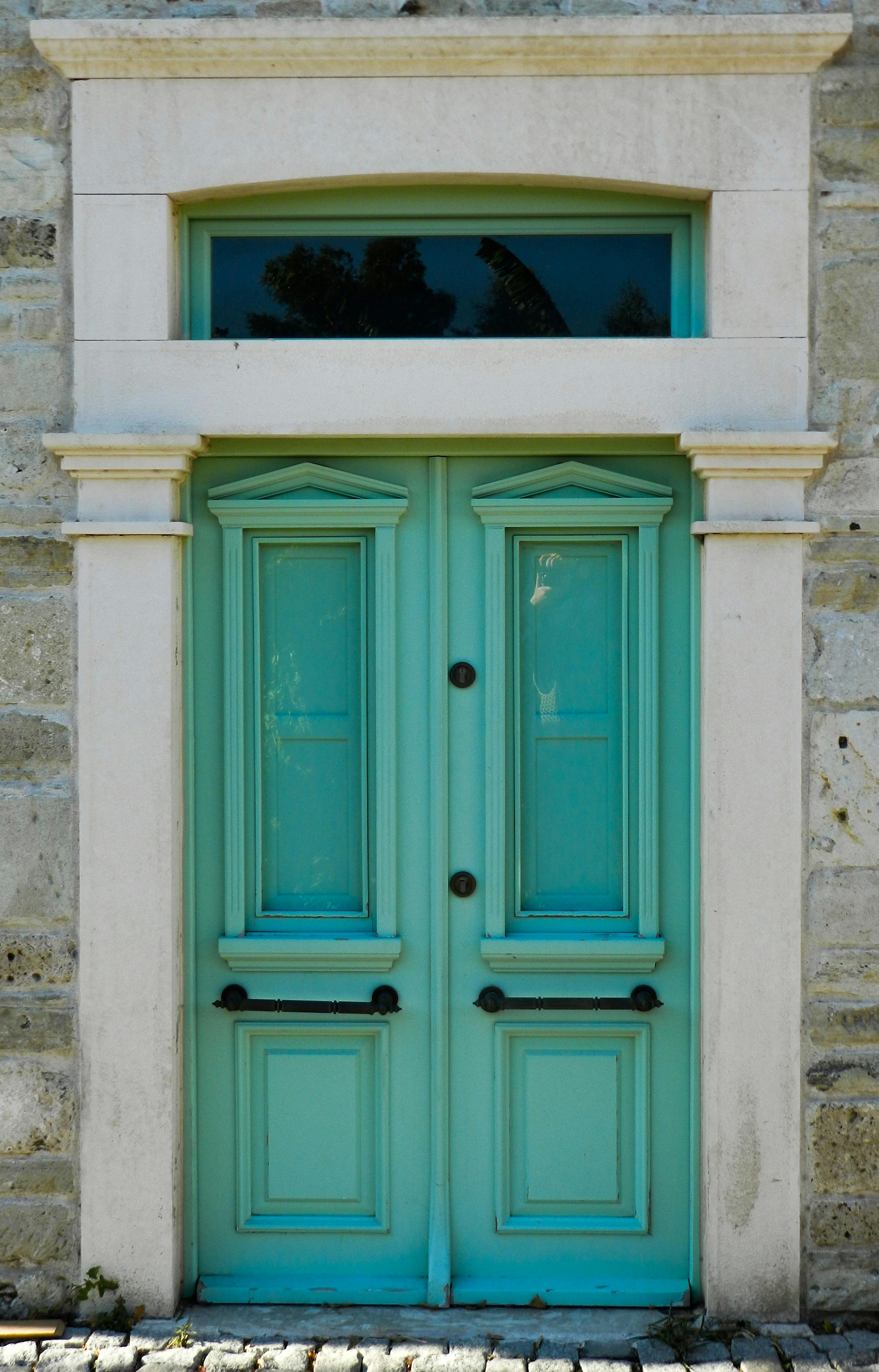 Classic turquoise double doors set in a stone wall, showcasing symmetry and vintage charm.