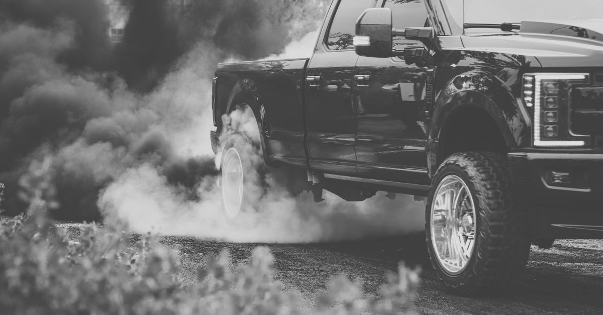 Black pickup truck emitting smoke during a burnout on the road.