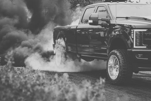 Black pickup truck emitting smoke during a burnout on the road.