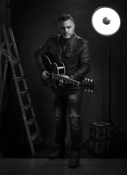 Black-and-white photo of a man playing an acoustic guitar in a studio setting.