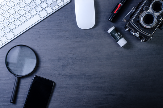 Flat lay of a vintage camera, keyboard, magnifying glass, and office supplies on a wooden desk surface.