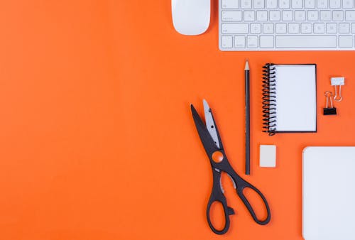 Close-Up Shot of a Keyboard beside School Supplies on an Orange Surface