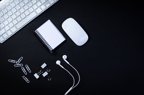 Earphones and Office Supplies Lying on Black Desk by Keyboa