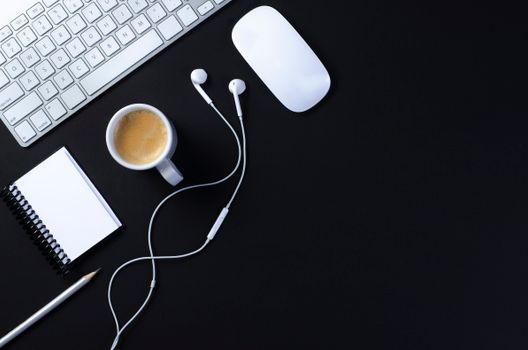 Flat lay of a modern workspace with coffee, keyboard, mouse, notebook, and headphones on a black surface.