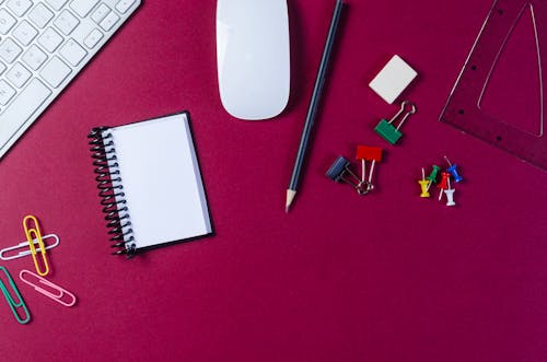 Close-Up Shot of a Keyboard beside School Supplies on a Red Surface