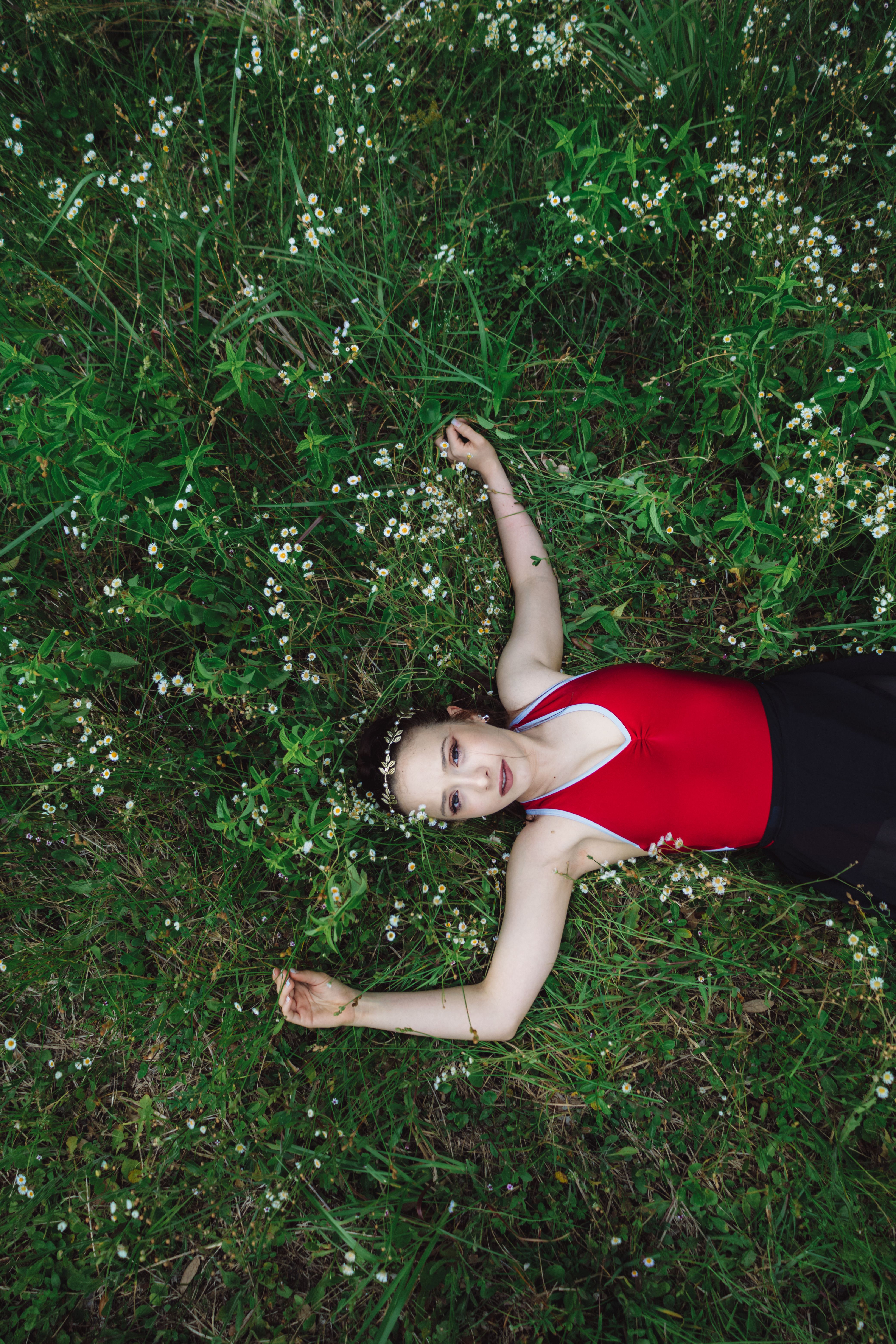 Woman in a red tank top relaxing on grass in an outdoor setting.