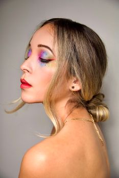 Artistic close-up portrait of a woman with vibrant, colorful makeup on neutral background.
