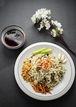 Minimalist presentation of Asian rice dish served with assorted sides and tea on a gray background.