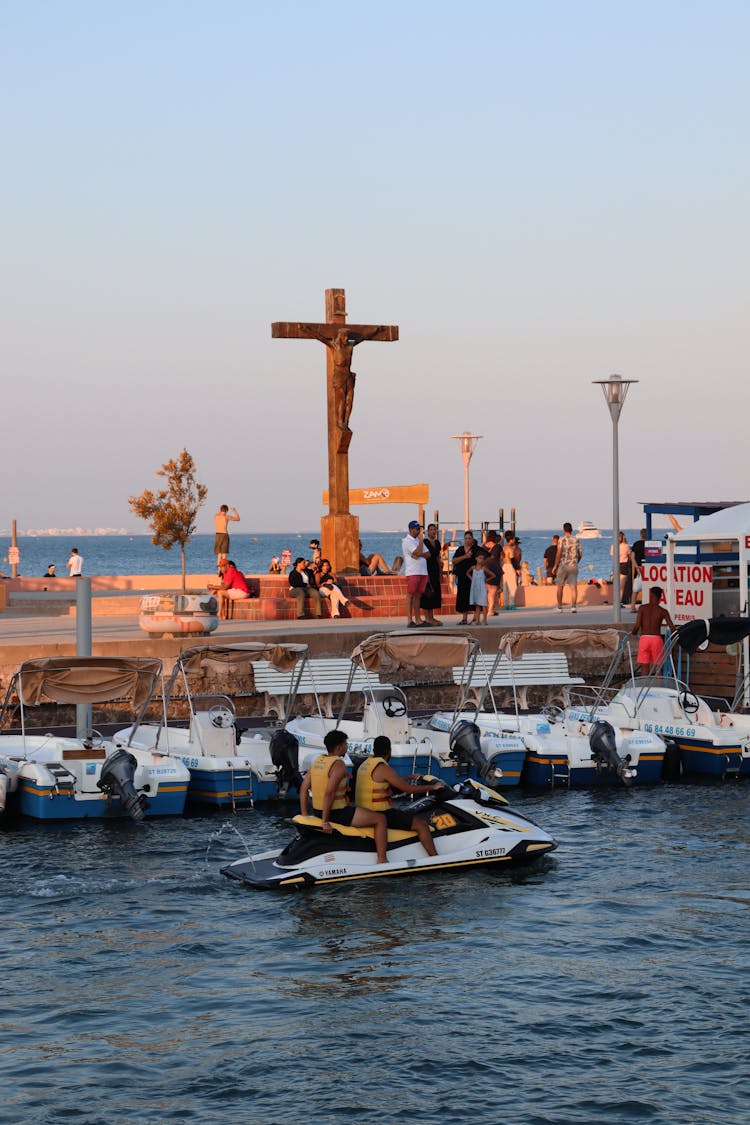 Religious Cross And People On A Pier At Dusk