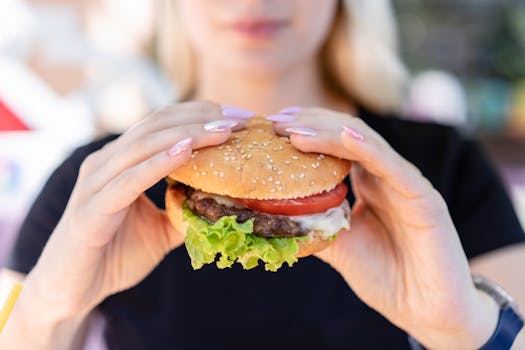 A close-up of a delicious burger with fresh ingredients held by a woman outdoors.