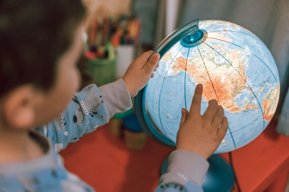 A child discovers geography by pointing at a globe, fostering curiosity and learning.