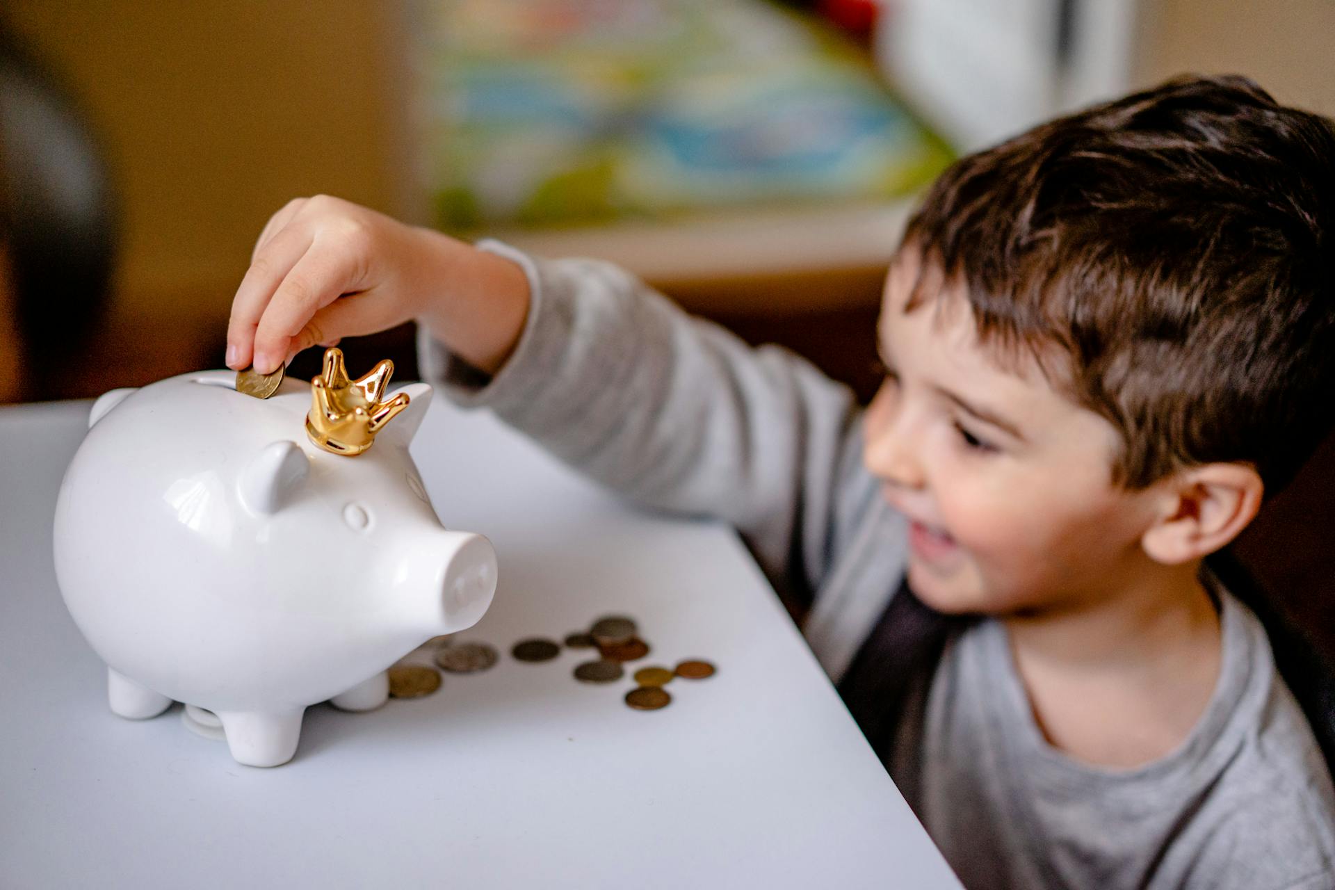 Young boy smiling while saving money in a crowned piggy bank, demonstrating financial responsibility.