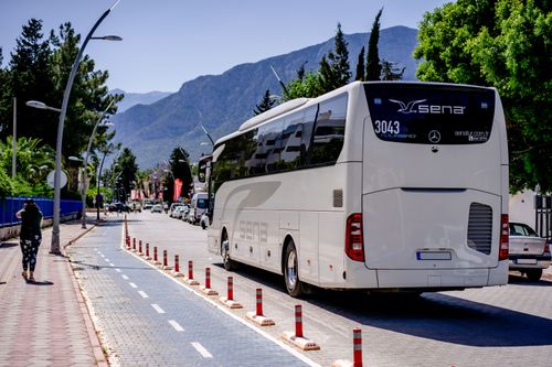 Free A white bus travels on a sunny mountain road lined with trees and sidewalks. Stock Photo