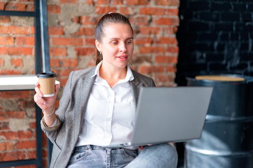 A Woman Using a Laptop while Holding a Cup of Coffee