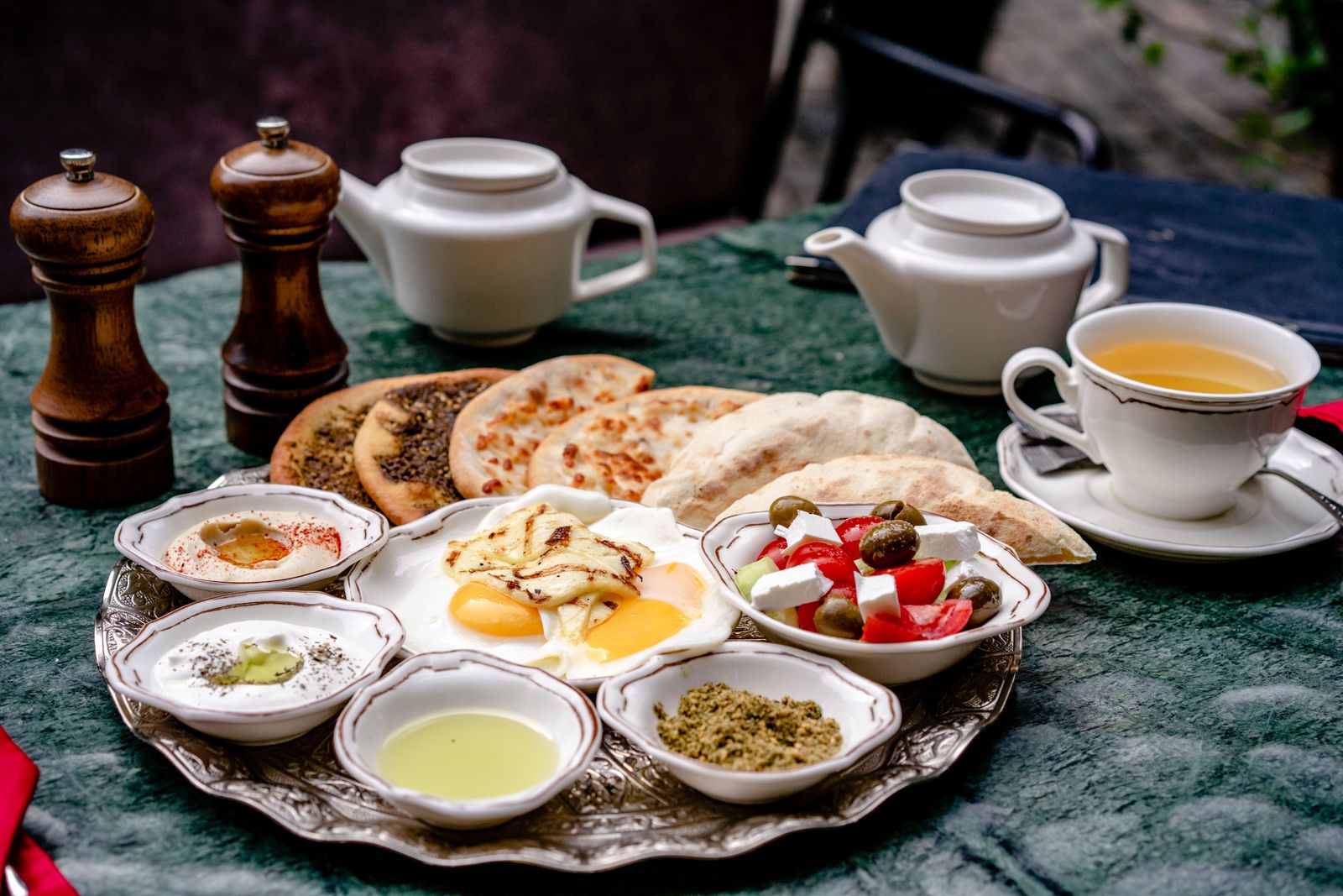 A breakfast spread of small bowls, eggs, flatbread and tea on an engraved silver tray