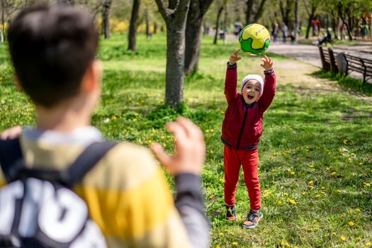 A joyful child in red jacket is playing catch with a ball in the sunny park.