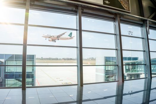 A plane in flight seen through airport terminal windows, reflecting air travel excitement.