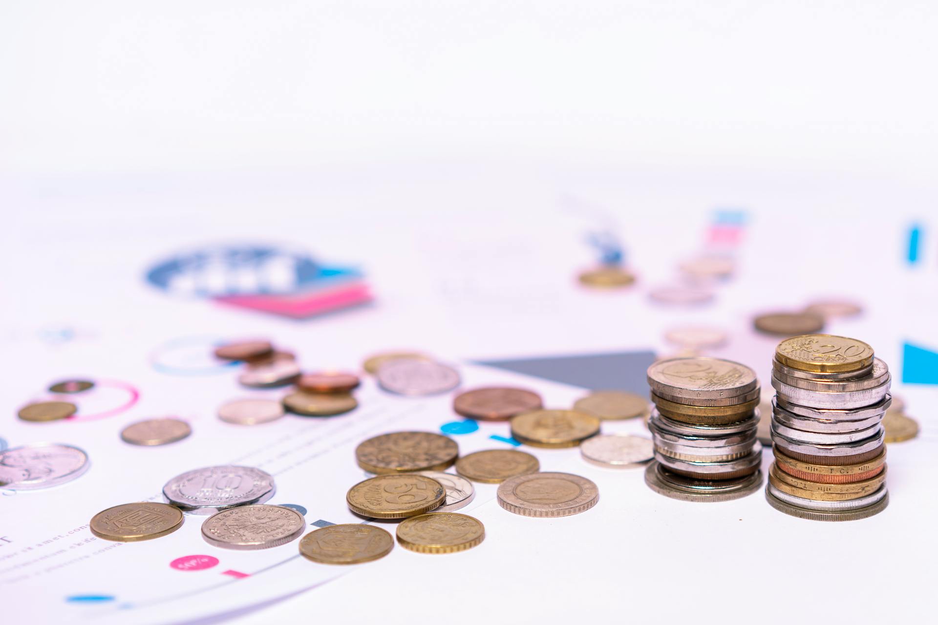 Stack of assorted coins with financial documents on a white background, highlighting the concept of savings.