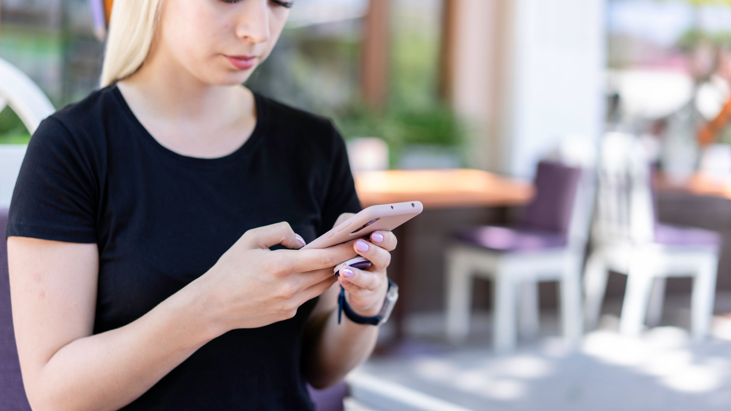 Young woman in a black shirt texting on her smartphone at an outdoor cafe.