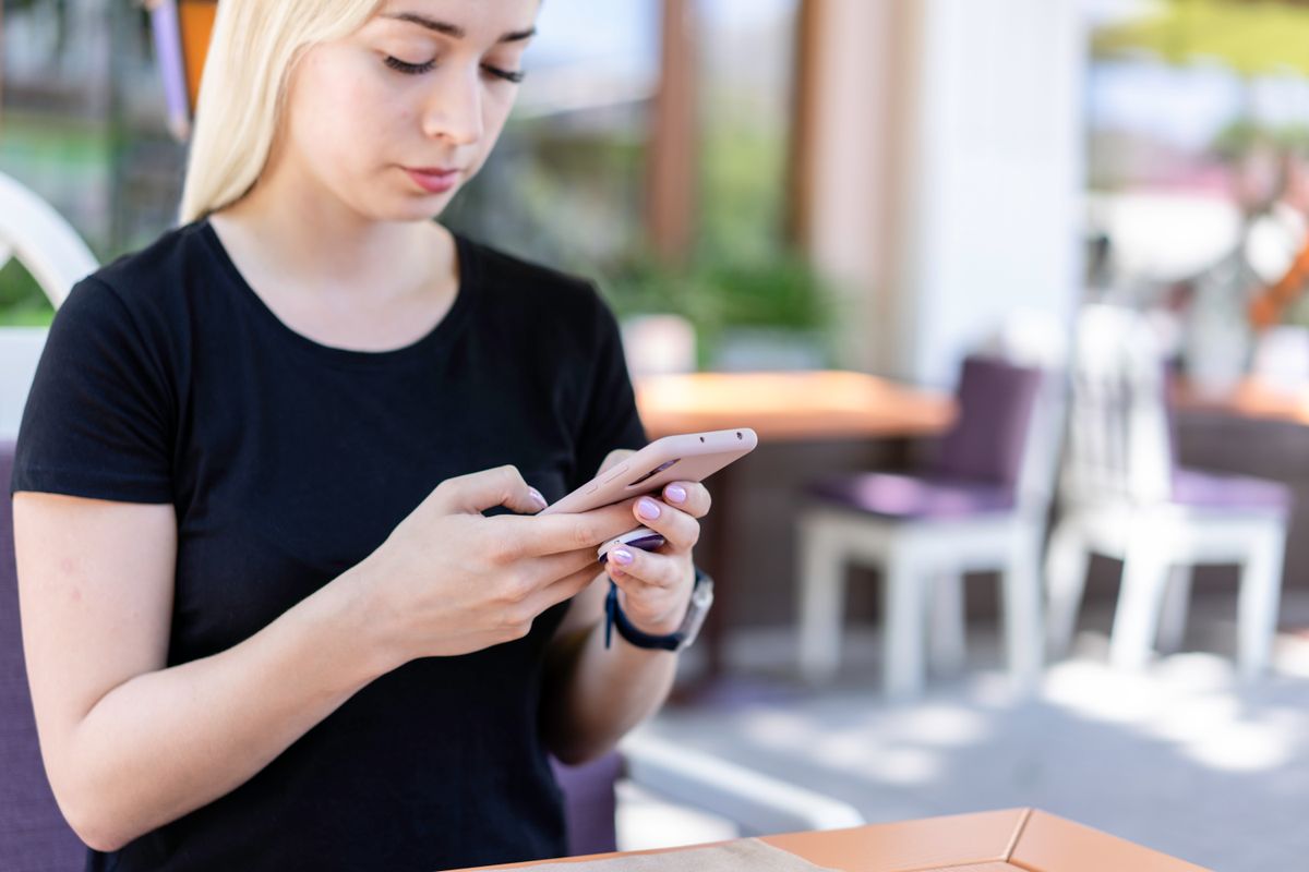 Mobil telefon tutan kişi açık hava kafede rahat oturmuş