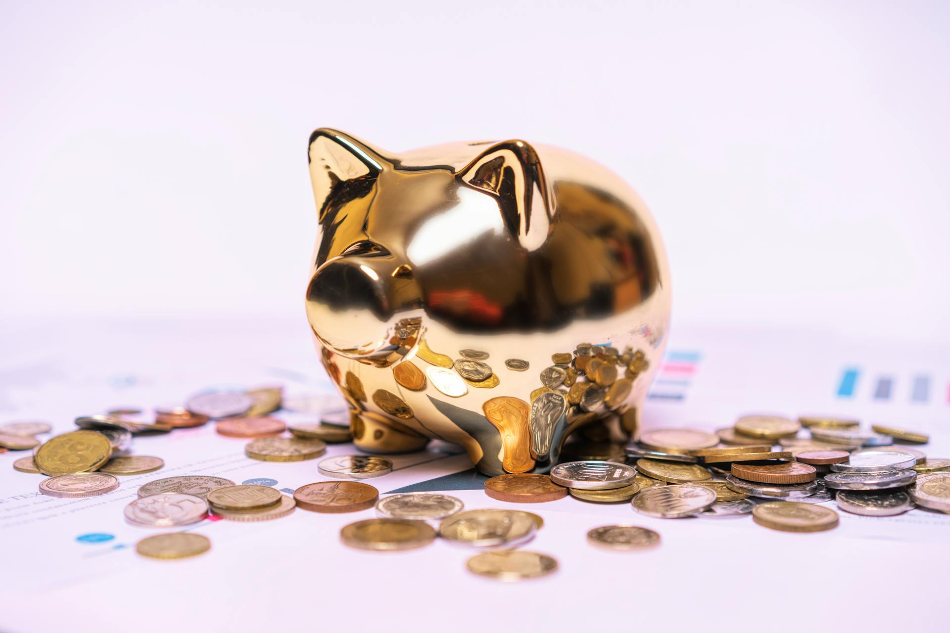 Shiny golden piggy bank on financial documents with scattered coins symbolizes savings.