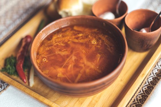 Earthenware bowl of red-orange shredded cabbage soup on a wooden tray with dried chili