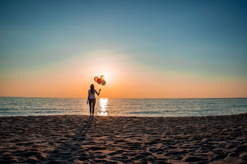 Woman Holding Balloons on the Beach at Sunset