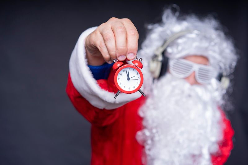 Santa Claus in sunglasses holding an alarm clock, capturing holiday humor and excitement.